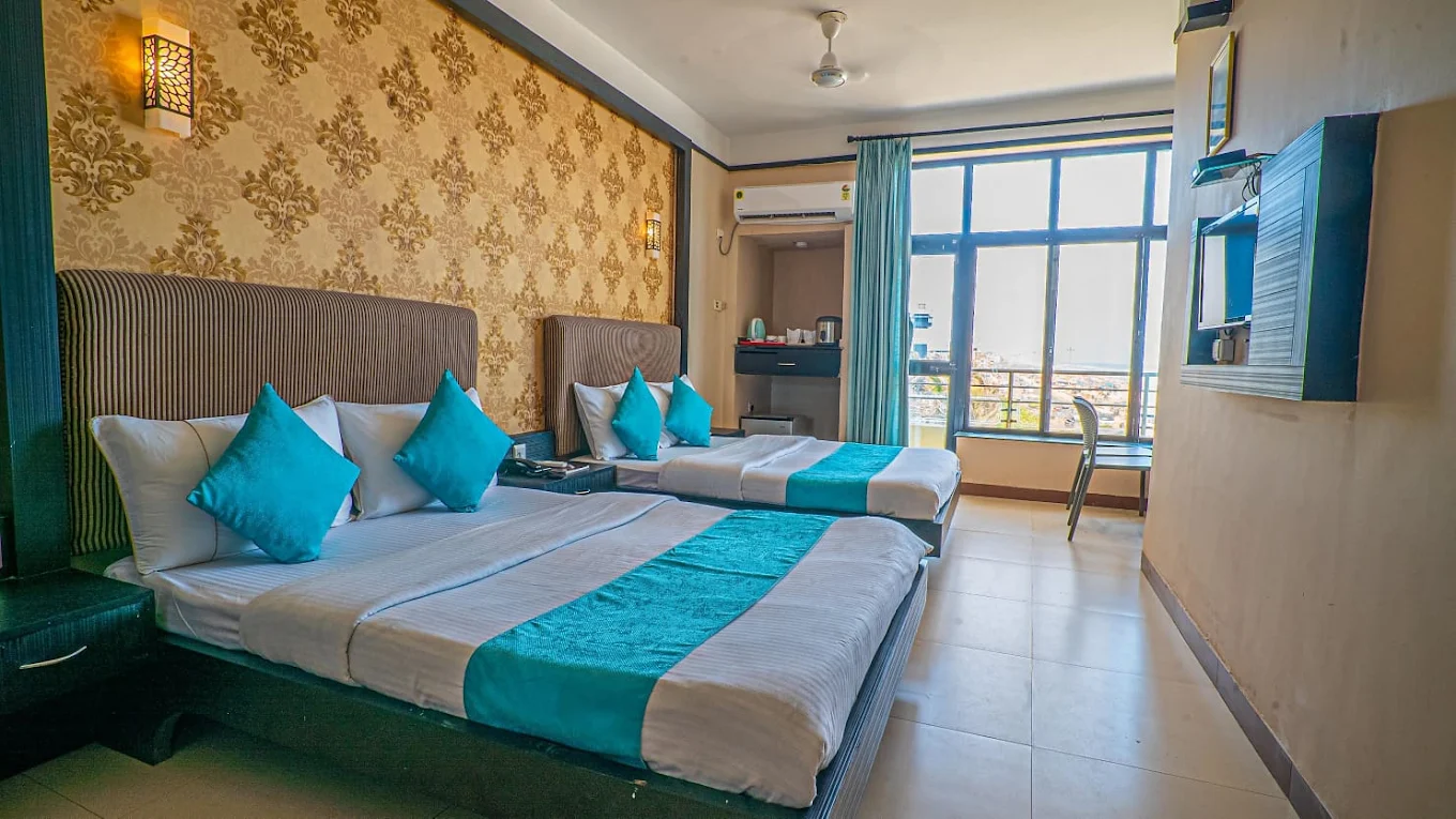 Room with two beds, turquoise cushions and a large window